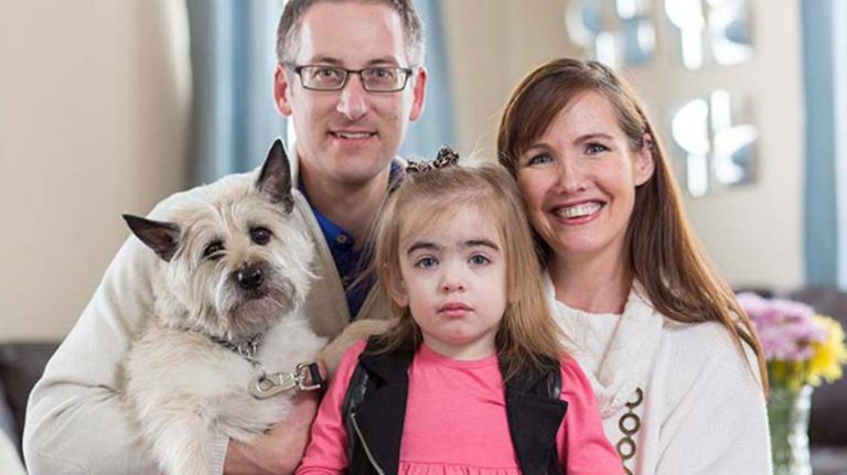 Color photo, family portrait of Reagan, a young girl with an orphan disease, her parents, and their dog