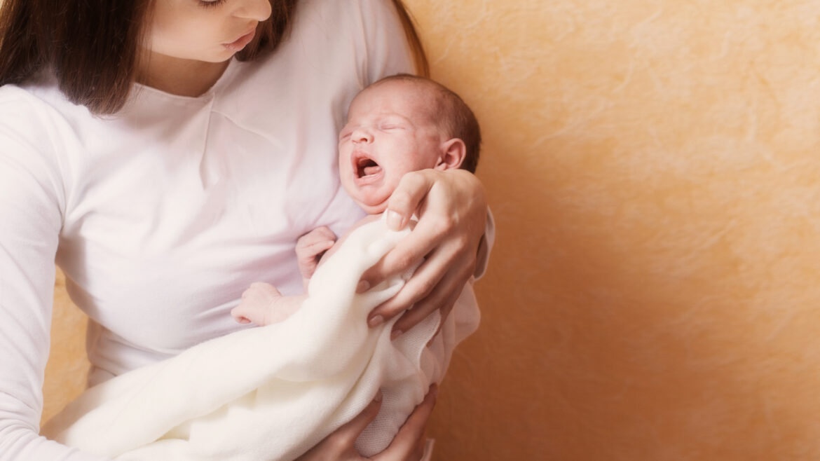 Infant crying in women's arms.