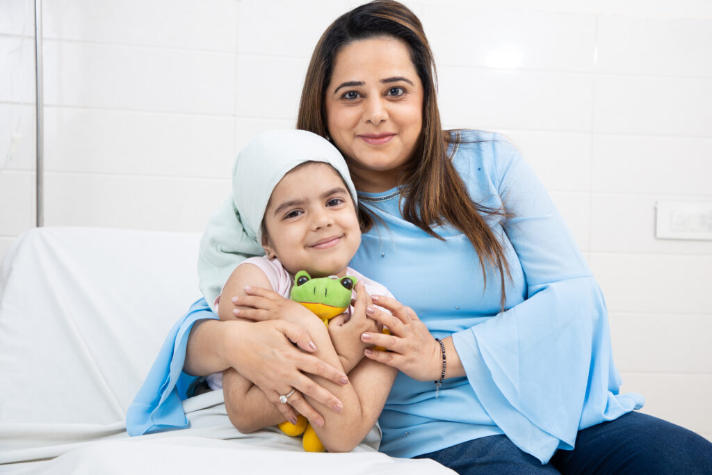 mother on a bed holding her young daughter who is smiling at the camera holding a toy frog
