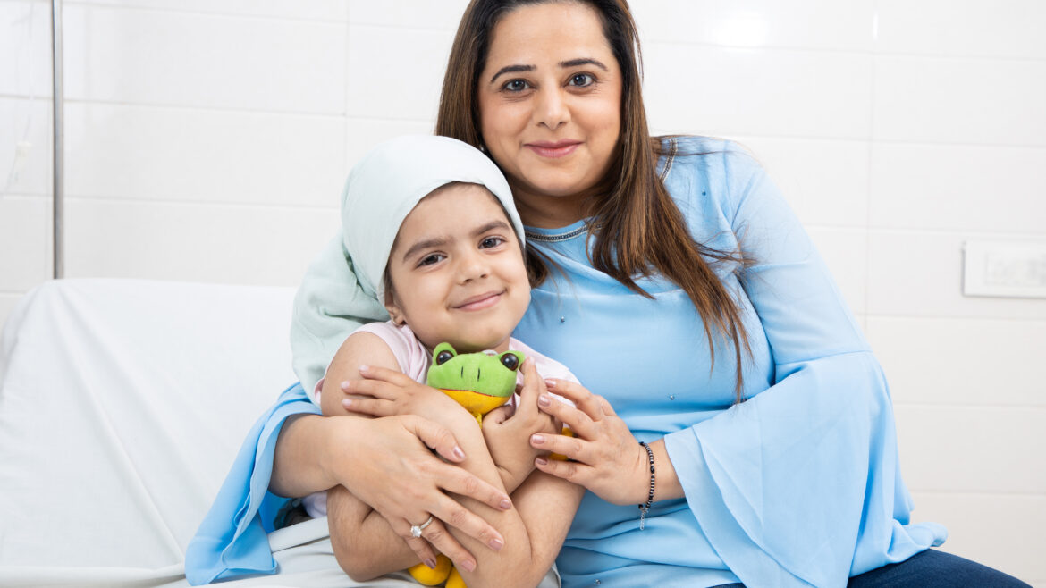mother on a bed holding her young daughter who is smiling at the camera holding a toy frog