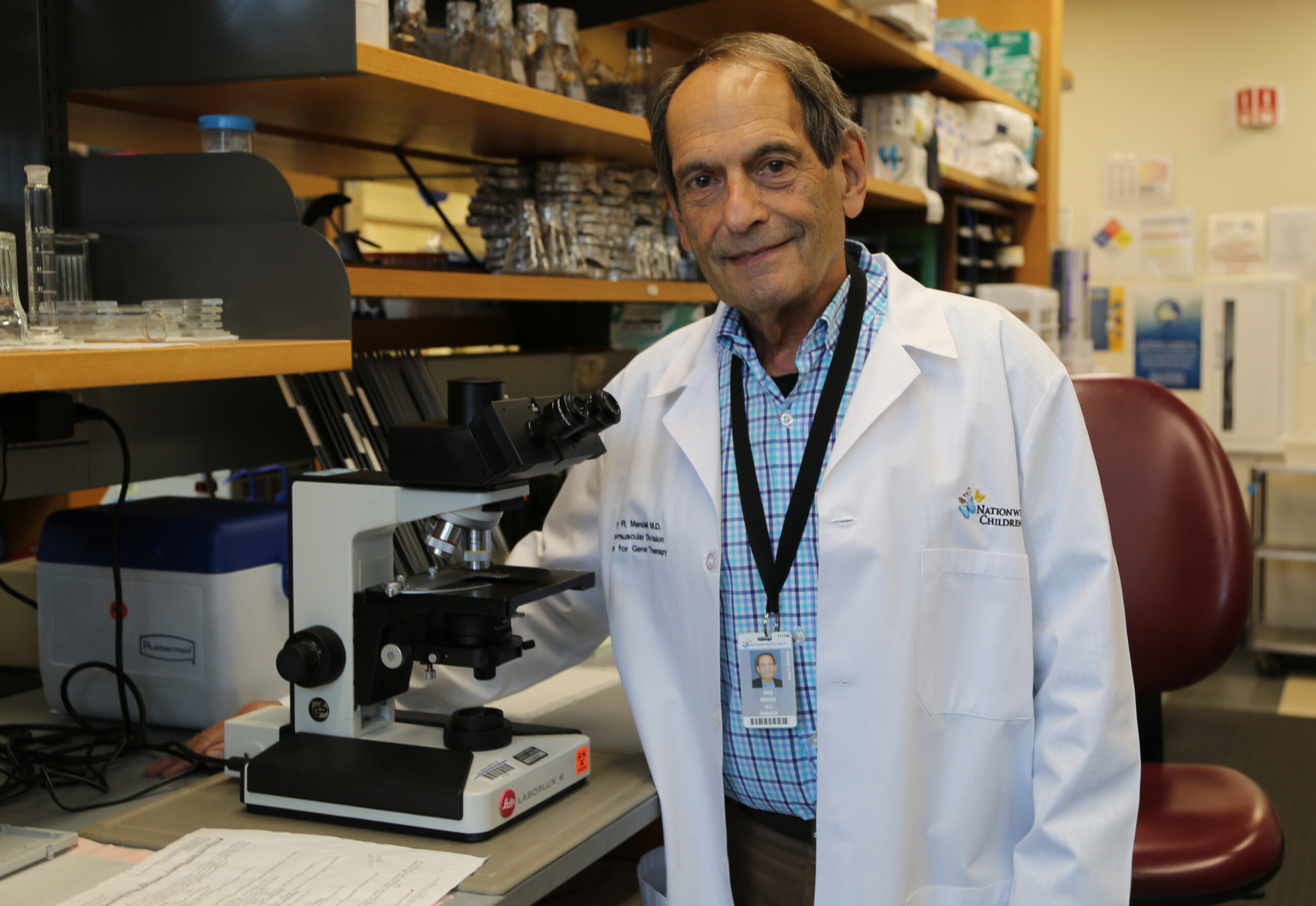 Dr. Jerry Mendell standing and smiling in a lab next to a microscope