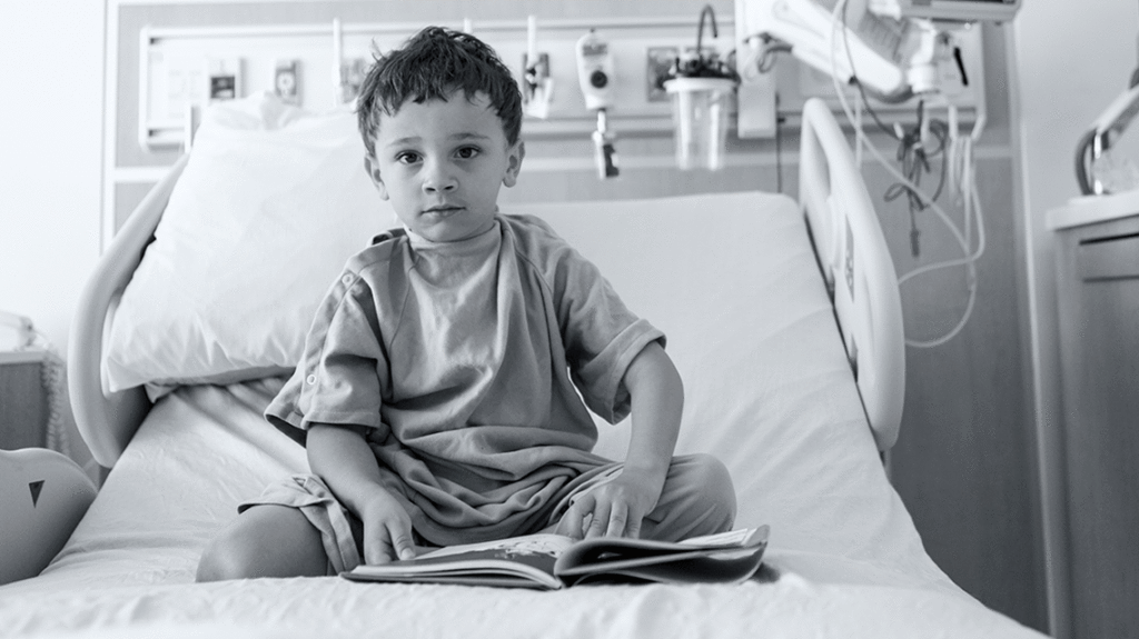 Black and white photo of boy sitting up on hospital bed