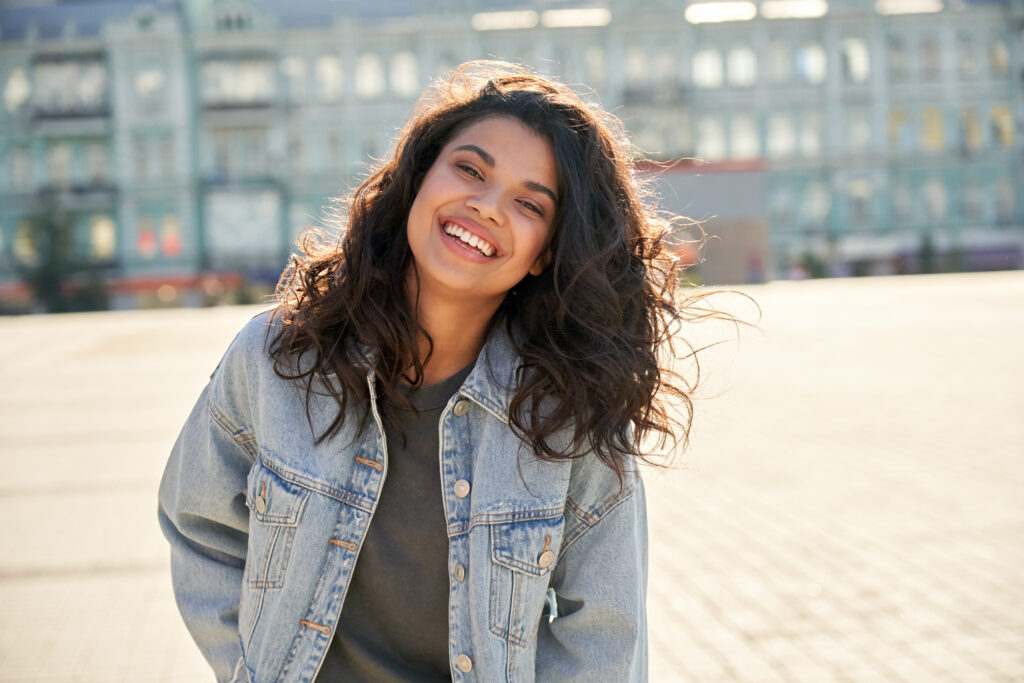 Teen girl smiling outside in sunny day wearing a jean jacket