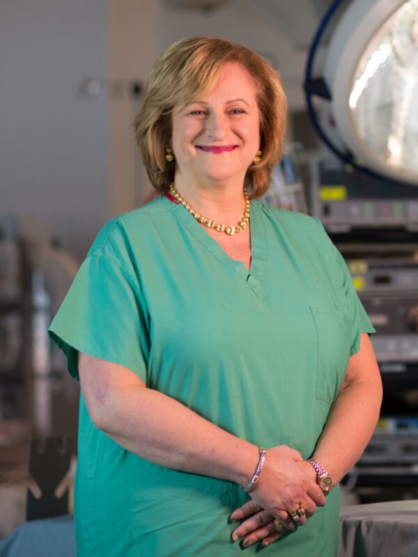 Dr. Gail Besner in an operating room wearing scrubs and smiling at the camera