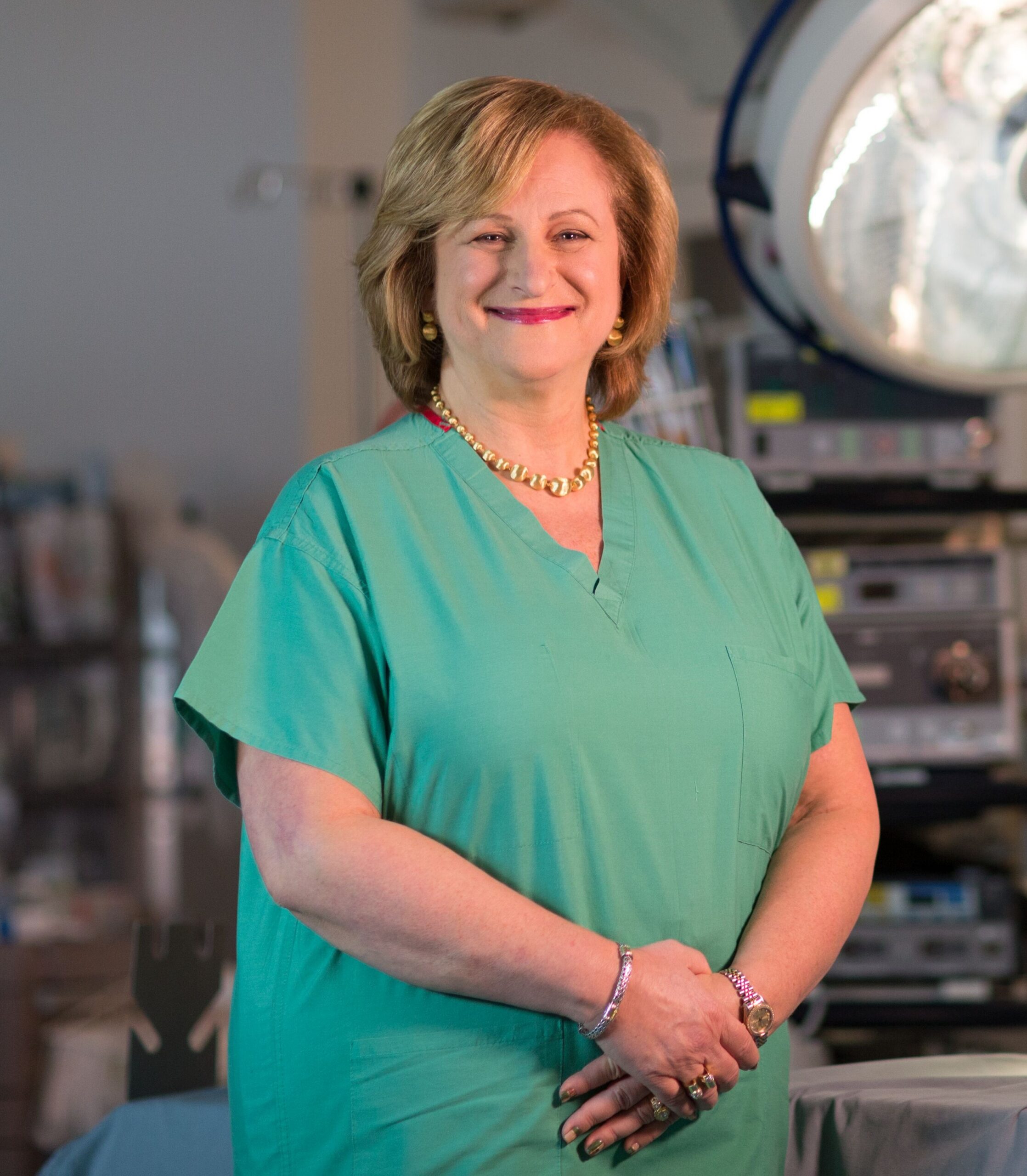 Dr. Gail Besner in an operating room wearing scrubs and smiling at the camera