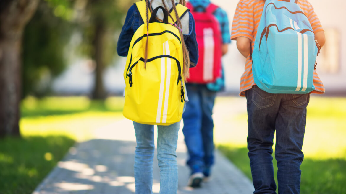 Three kids walking away with backpacks on a sunny day on a sidewalk