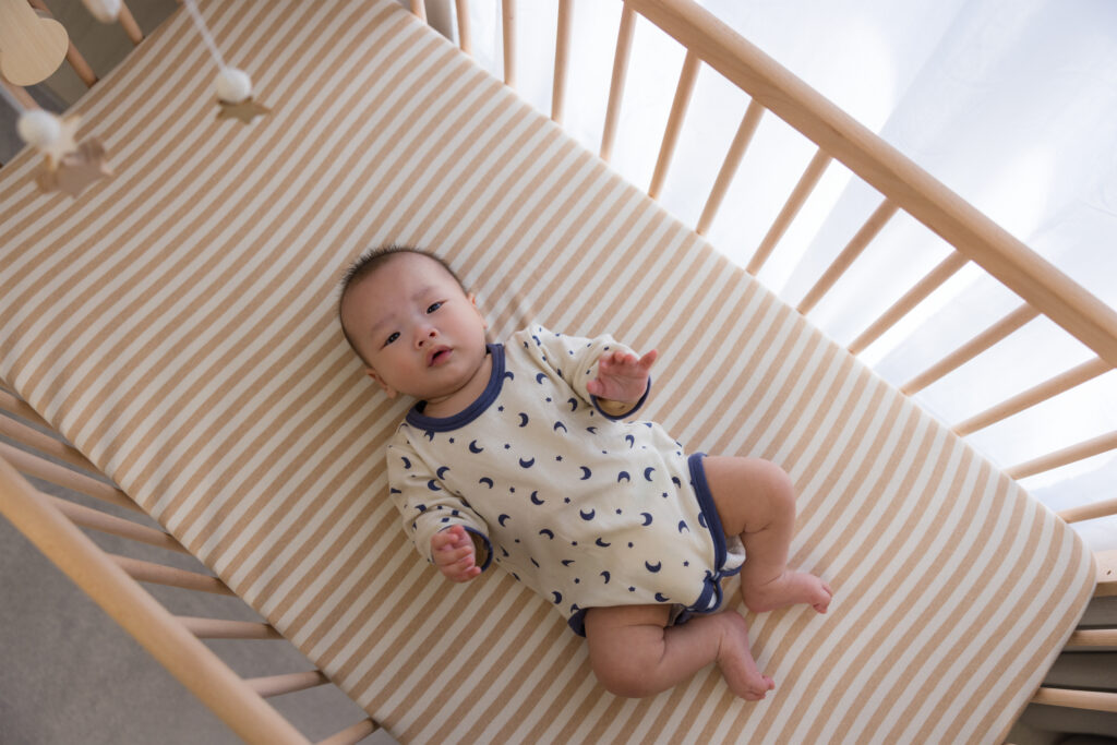 Baby laying in a wooden crib looking up at the camera
