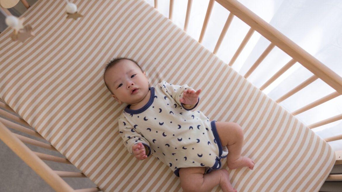 Baby laying in a wooden crib looking up at the camera
