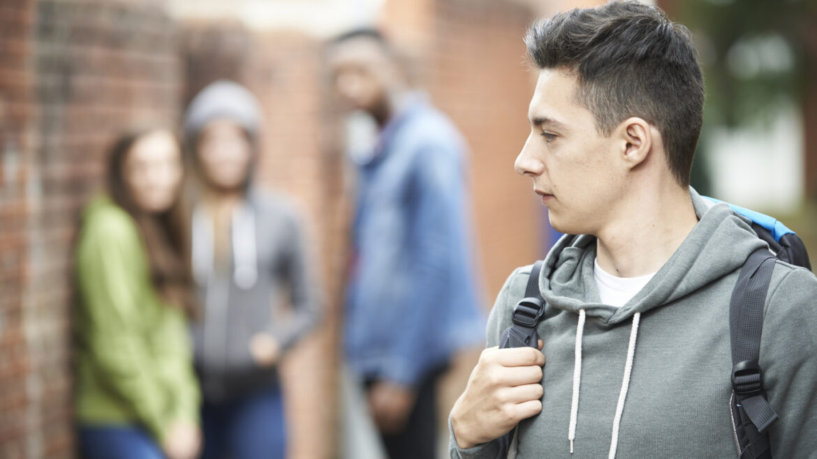 Teenage male in a grey hoody and a backpack looking back at a group of teens