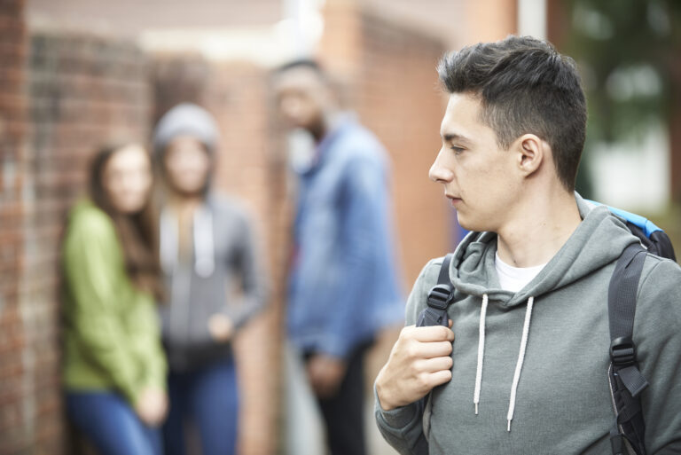 Teenage male in a grey hoody and a backpack looking back at a group of teens
