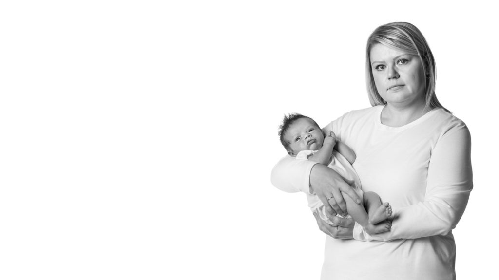 Black and white image of an unsmiling White woman holding a young, awake infant in the right third of the frame