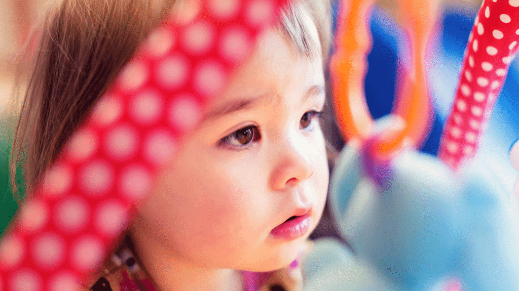 Color close up image of young baby girl looking at hanging toys