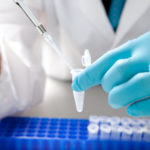 close up of a researcher with blue gloves inject liquid into vials.