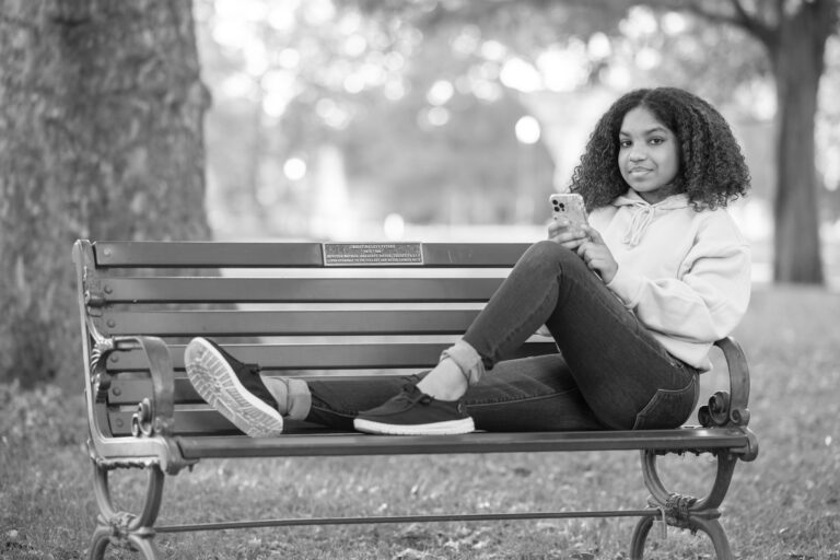 Girl sitting on a bench with her phone smiling.