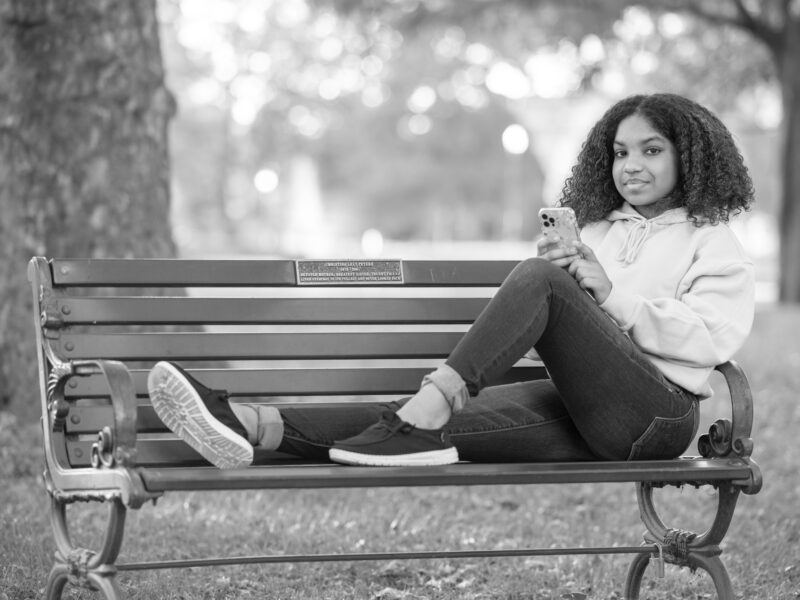 Girl sitting on a bench with her phone smiling.