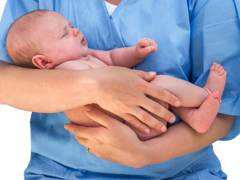 person in blue scrubs holding a baby, cropped so focus is on the baby