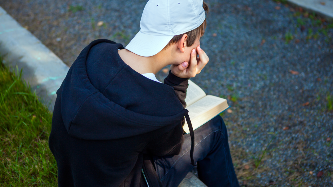 teen boy with back to camera reading a book
