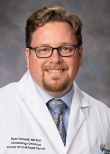Studio portrait of Ryan Roberts, MD, PhD, wearing a white coat, blue shirt and blue tie