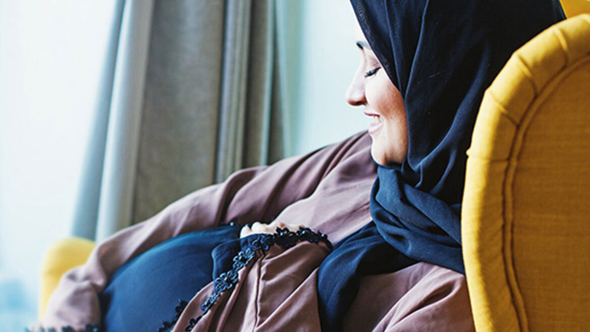 Pregnant woman smiling and holding her belly while awaiting a fetal echocardiogram to check her baby’s heart health during pregnancy.