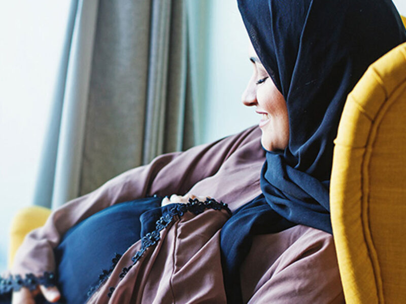 Pregnant woman smiling and holding her belly while awaiting a fetal echocardiogram to check her baby’s heart health during pregnancy.