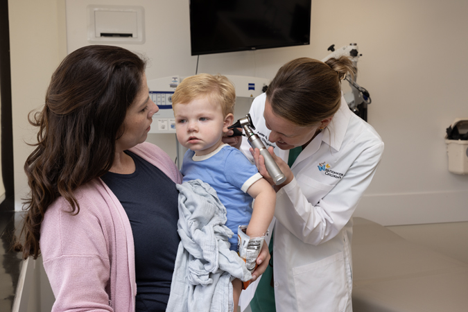Pediatric patient at a follow-up appointment after in-office ear tube insertion, with a doctor examining the child’s ear while the mother provides support.