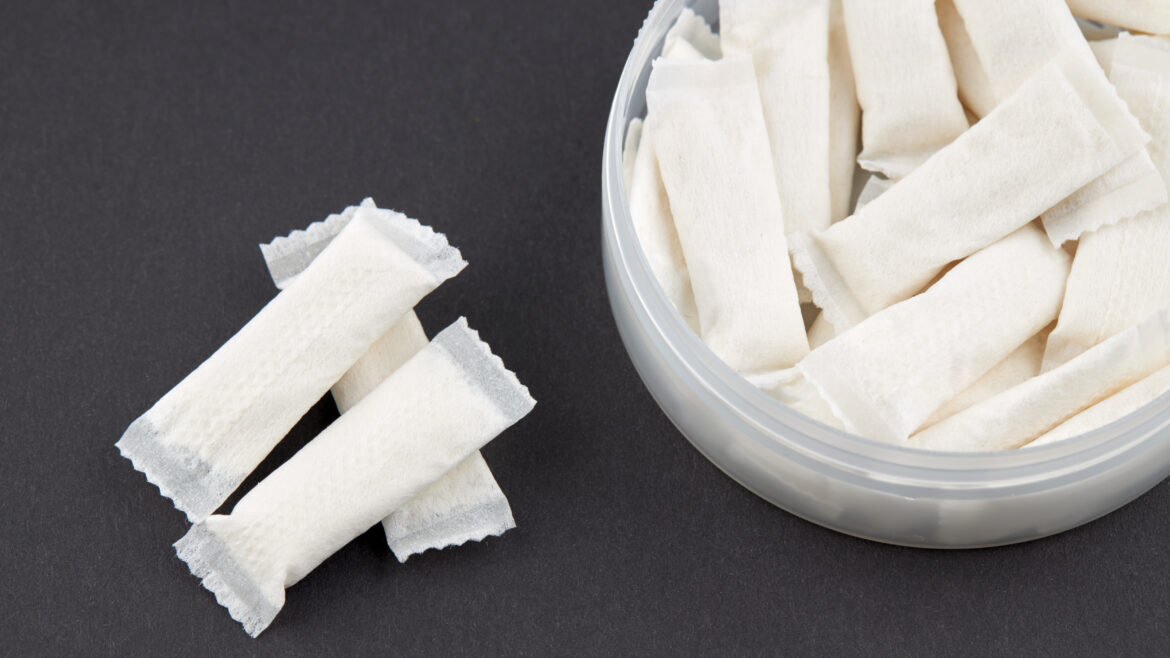 Close-up of nicotine pouches in a plastic container on a dark background, illustrating smokeless tobacco alternatives and nicotine addiction and poisoning risks.