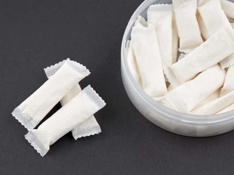 Close-up of nicotine pouches in a plastic container on a dark background, illustrating smokeless tobacco alternatives and nicotine addiction and poisoning risks.