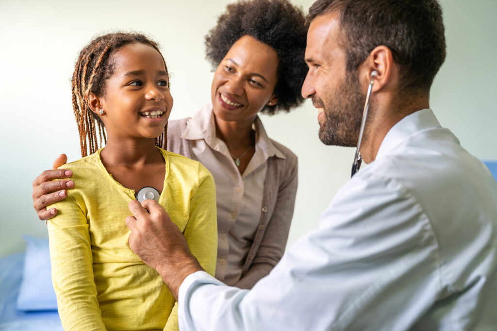 Young pediatrician examining a little African-American girl at hospital. Health care, people concept