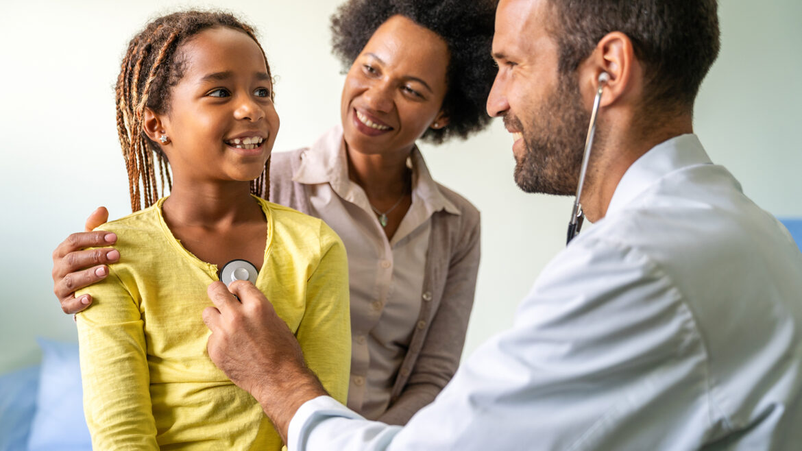 Young pediatrician examining a little African-American girl at hospital. Health care, people concept