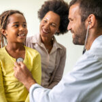 Young pediatrician examining a little African-American girl at hospital. Health care, people concept