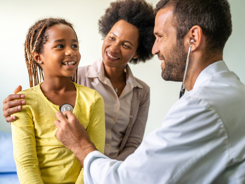 Young pediatrician examining a little African-American girl at hospital. Health care, people concept