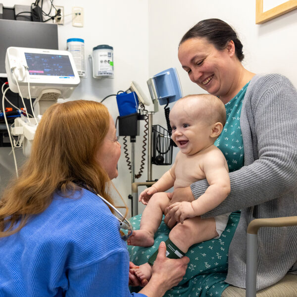 Baby being held by his mother while a doctor interacts with him for a check up.
