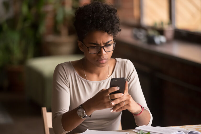 Upset confused Black woman holding cellphone having problem with mobile phone, frustrated angry mixed race girl reading bad news in message looking at smartphone annoyed by spam or missed call