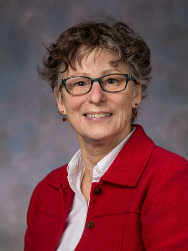 Portrait of Susan Reynolds, PhD, wearing glasses, a white shirt and red jacket
