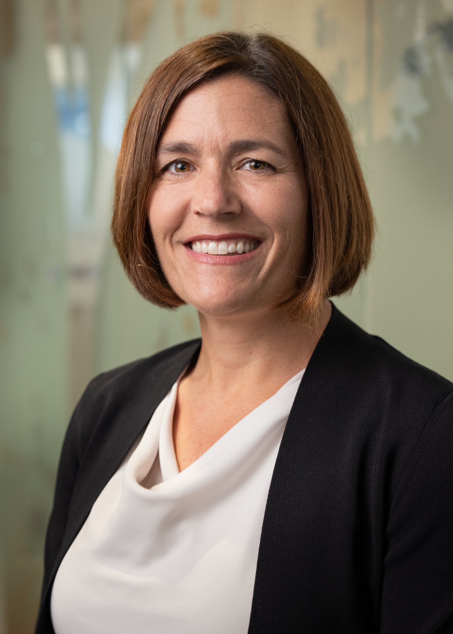Color portrait of Dr. Sara Bode, wearing a black blazer and white blouse, smiling at the camera