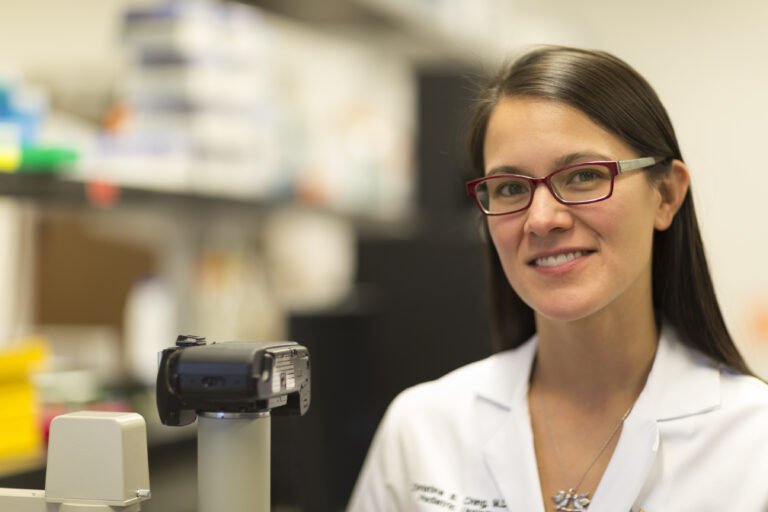 Photo of Christina Ching, MD, wearing a white lab coat, smiling at the camera in a lab.