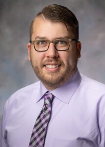 Studio portrait of Eric Mull, MD, wearing a lavender shirt and purple checked tie.