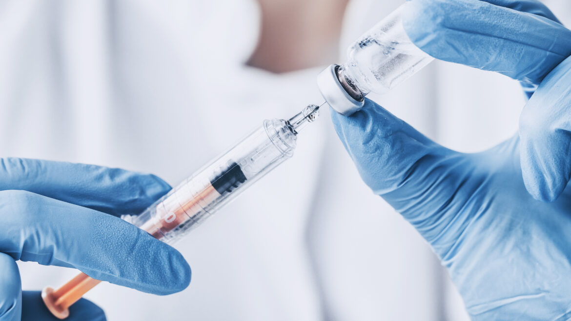 Close up of gloved doctor's hands injecting vaccine medicine into a syringe - stock image