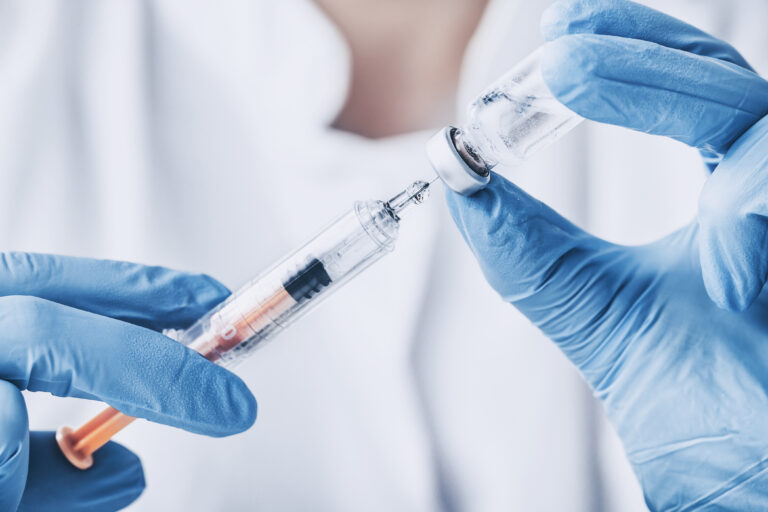 Close up of gloved doctor's hands injecting vaccine medicine into a syringe - stock image