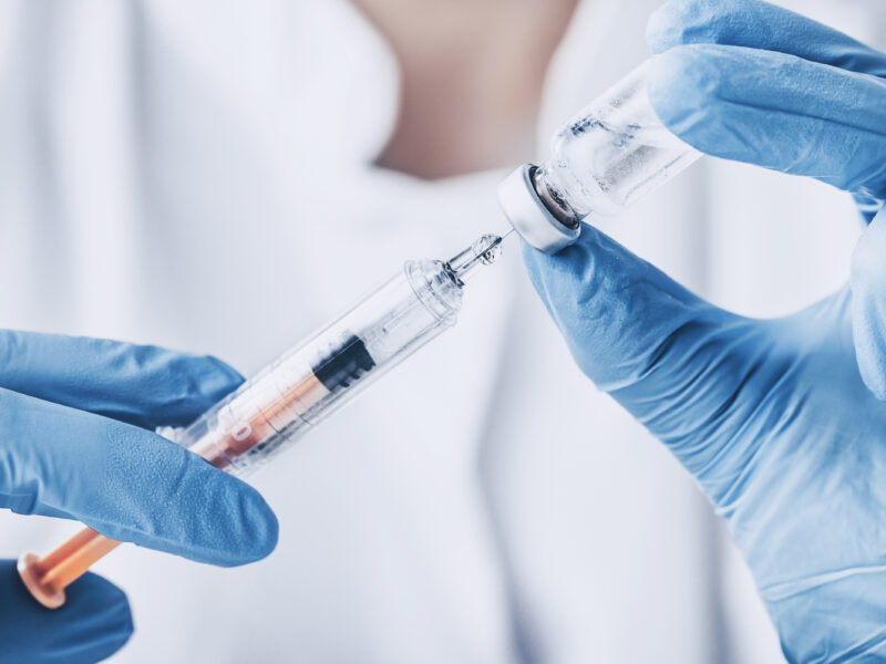 Close up of gloved doctor's hands injecting vaccine medicine into a syringe - stock image
