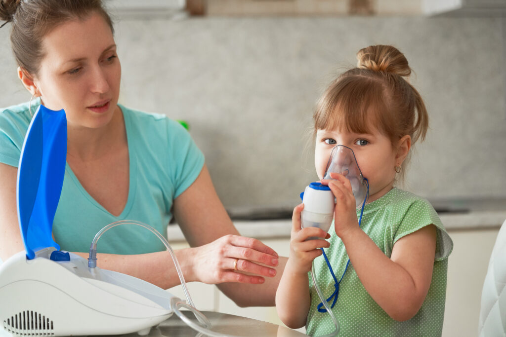a woman makes inhalation to a child at home. brings the nebulizer mask to his face. inhales the vapor of the medication. the girl is breathing through a mask