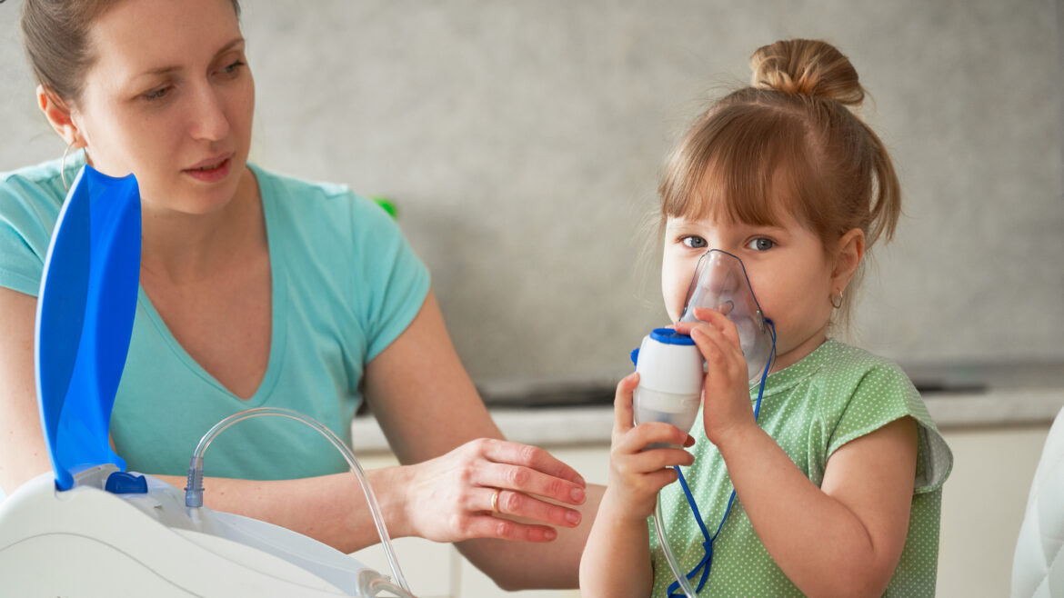 a woman makes inhalation to a child at home. brings the nebulizer mask to his face. inhales the vapor of the medication. the girl is breathing through a mask