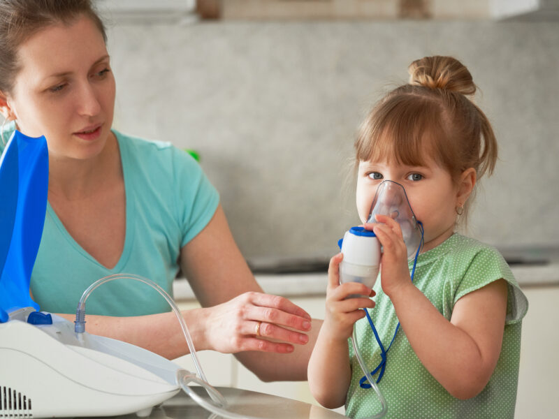 a woman makes inhalation to a child at home. brings the nebulizer mask to his face. inhales the vapor of the medication. the girl is breathing through a mask