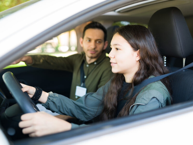 Caucasian adolescent girl paying attention to the road and listening to her instructor. Teenage girl driving during her test to get a driver's license