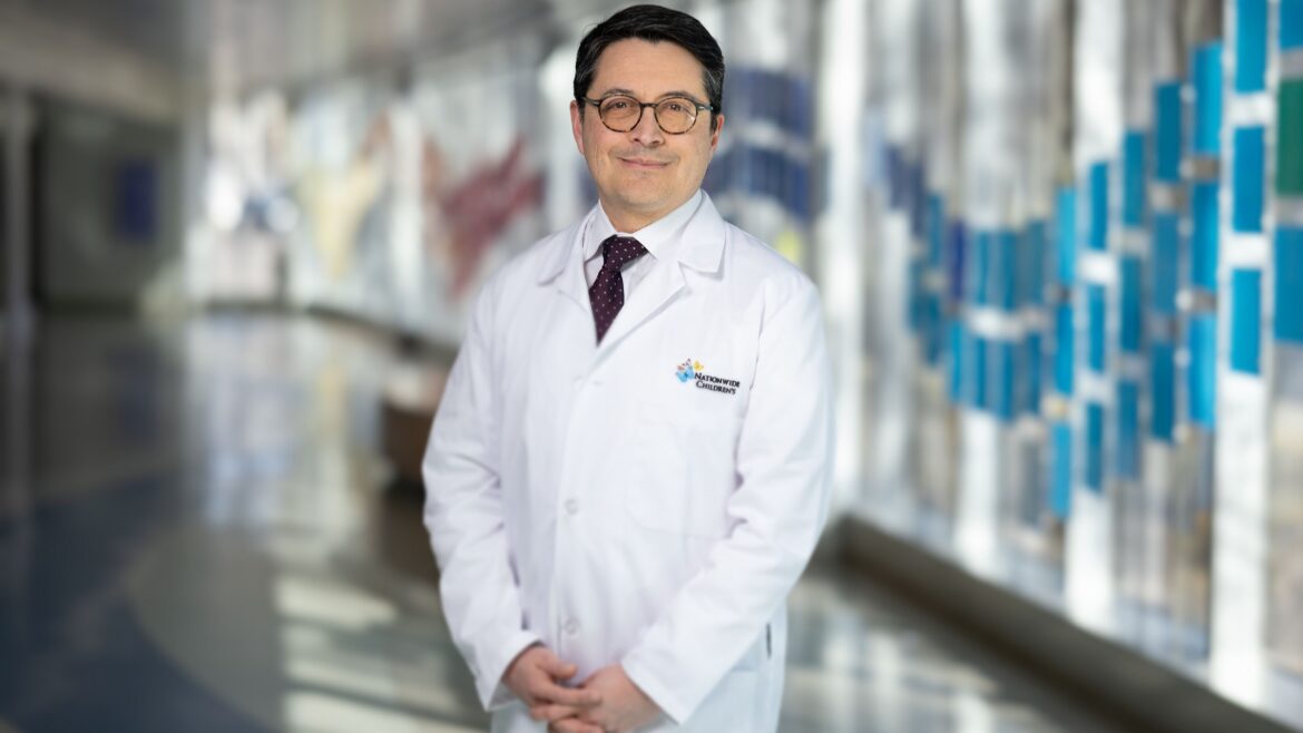 Antonio Cabrera, MD, wearing white coat and tie standing in hospital hallway