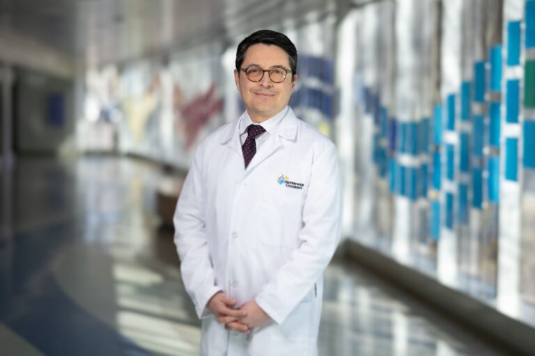 Antonio Cabrera, MD, wearing white coat and tie standing in hospital hallway