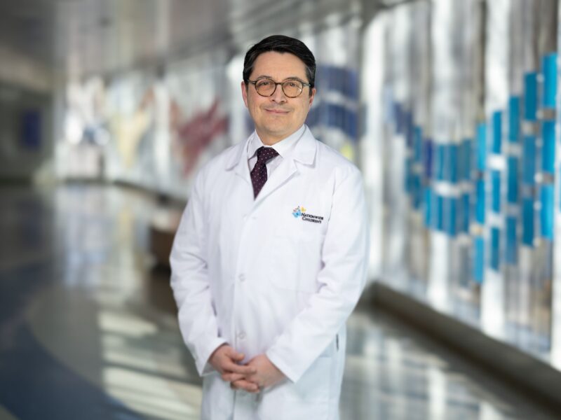 Antonio Cabrera, MD, wearing white coat and tie standing in hospital hallway