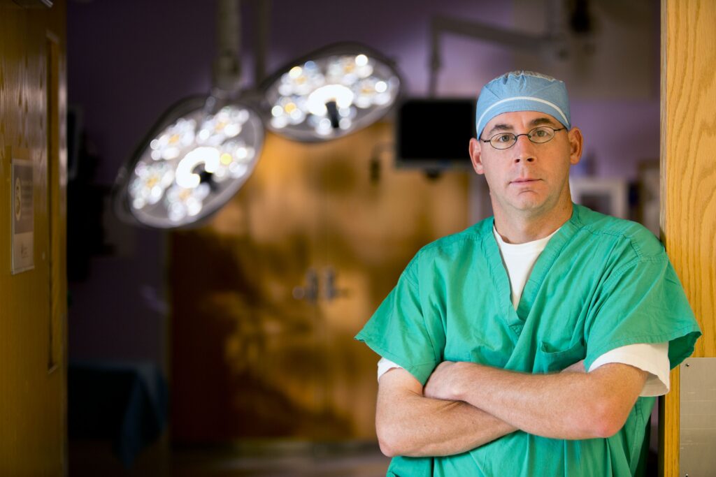 Dr. Kevin E. Klingele, MD standing in a doorway, wearing green surgery scrubs, crossing his arms looking at the camera.