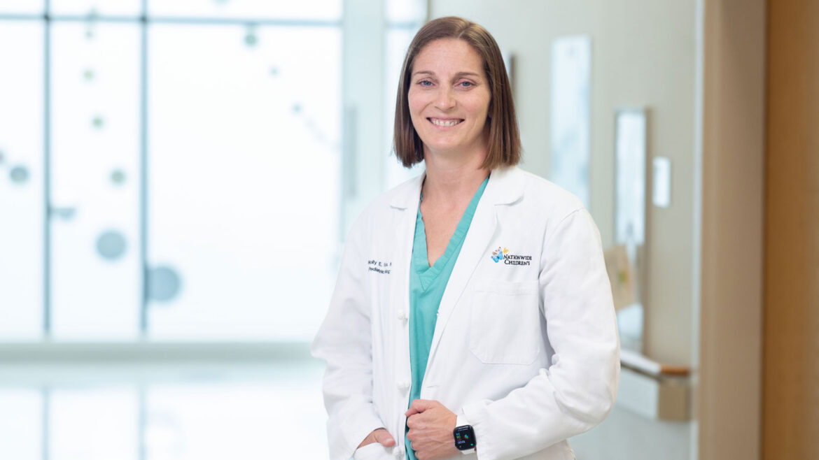 Molly Fuchs, MD, chief of Urology at Nationwide Children's, wearing scrubs and a white coat standing in a hospital hallway.