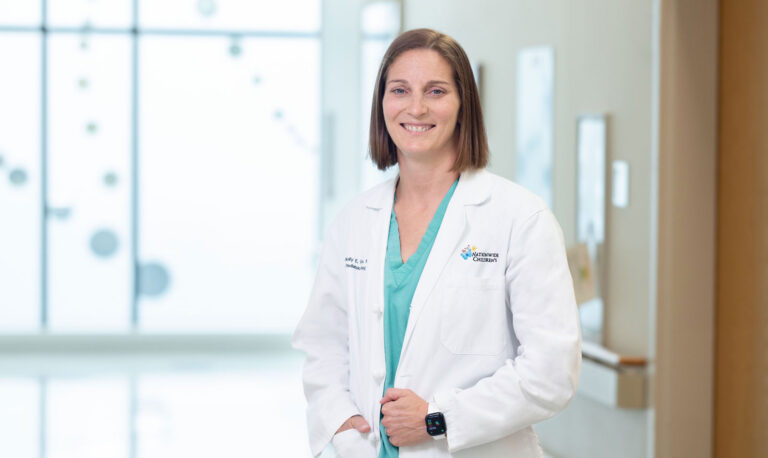 Molly Fuchs, MD, chief of Urology at Nationwide Children's, wearing scrubs and a white coat standing in a hospital hallway.
